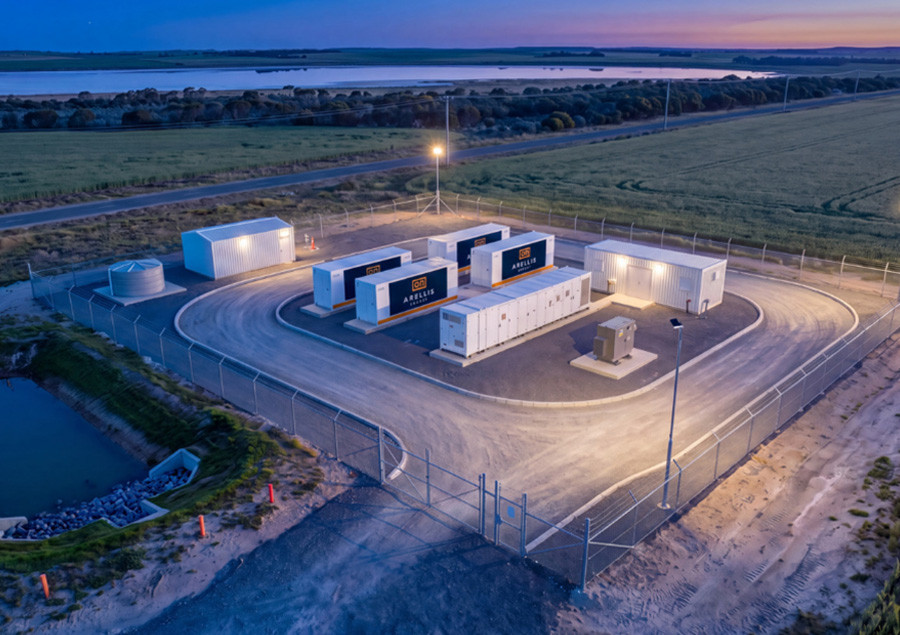 Community battery site lit at twilight, with farmland and water beyond