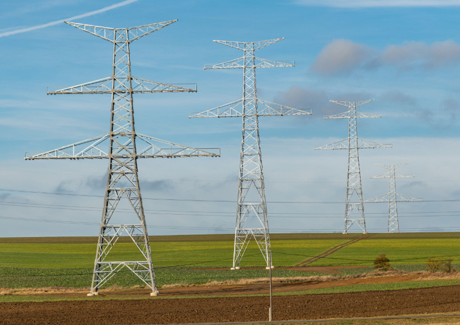 High-voltage transmission towers crossing open farmland under a blue sky