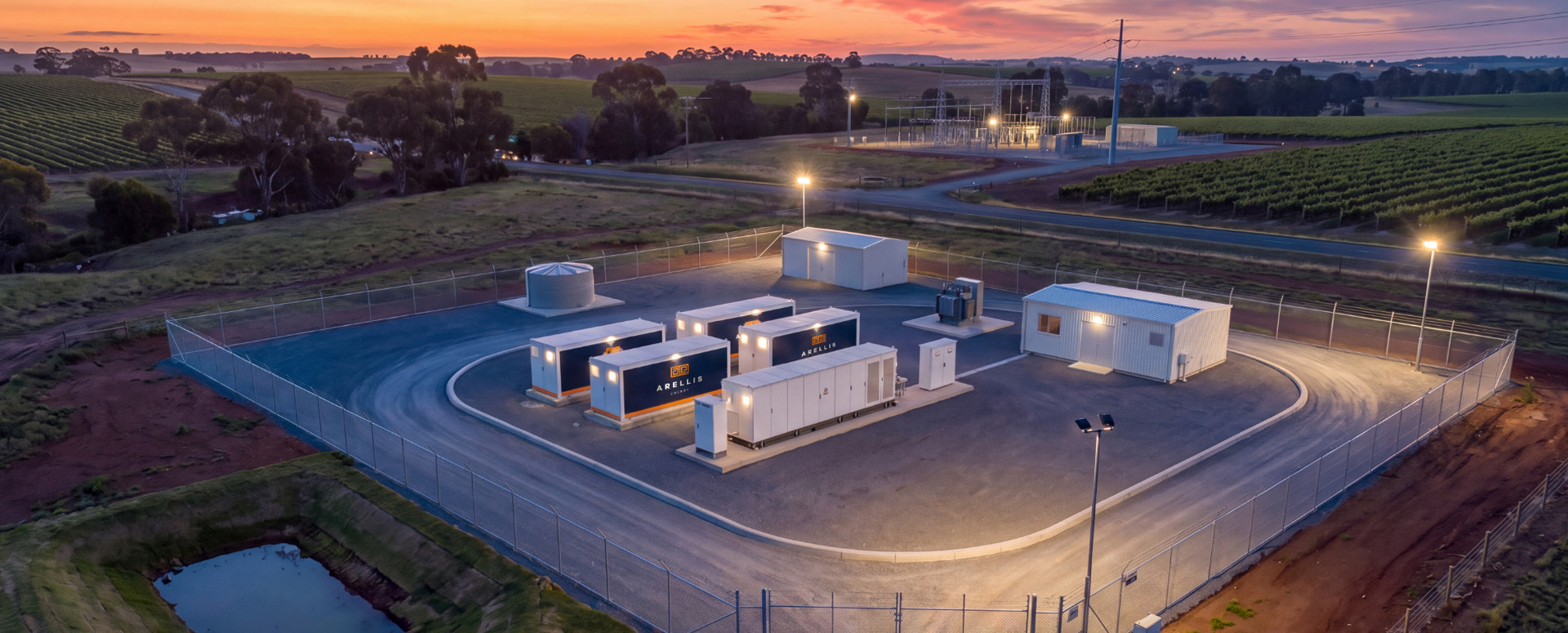 Lit community battery compound surrounded by vineyards at sunset